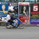 A motorcyclist rides past posters of candidates for the upcoming mayoral elections in Bangkok